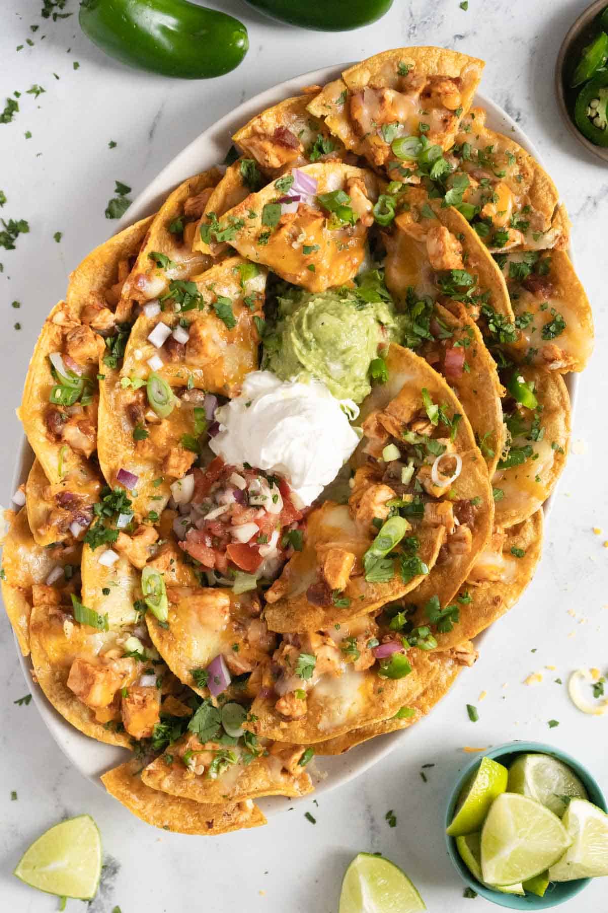 Chicken nachos on a plate with slices of limes. 
