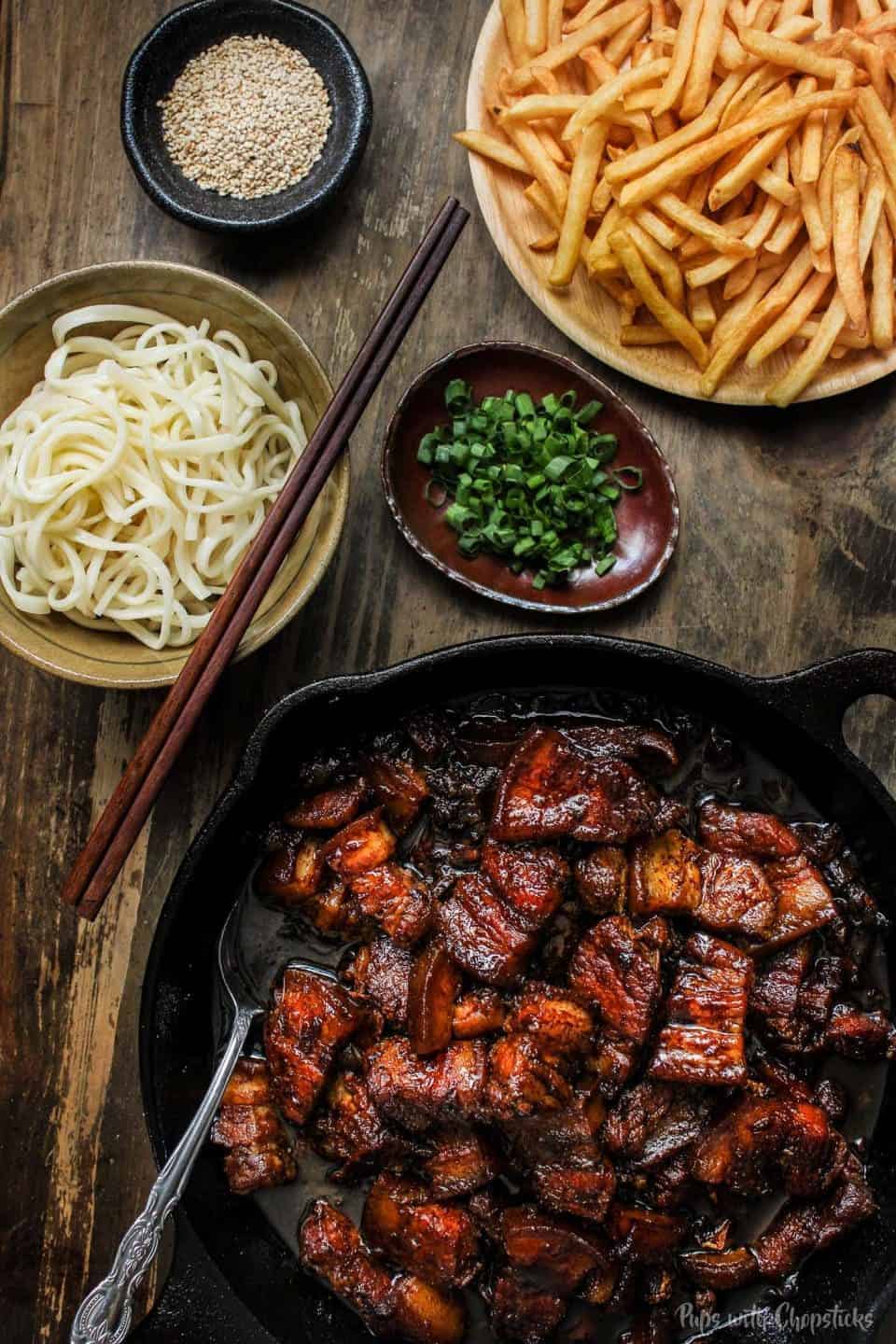 A pork belly skillet with noodles and chopsticks.
