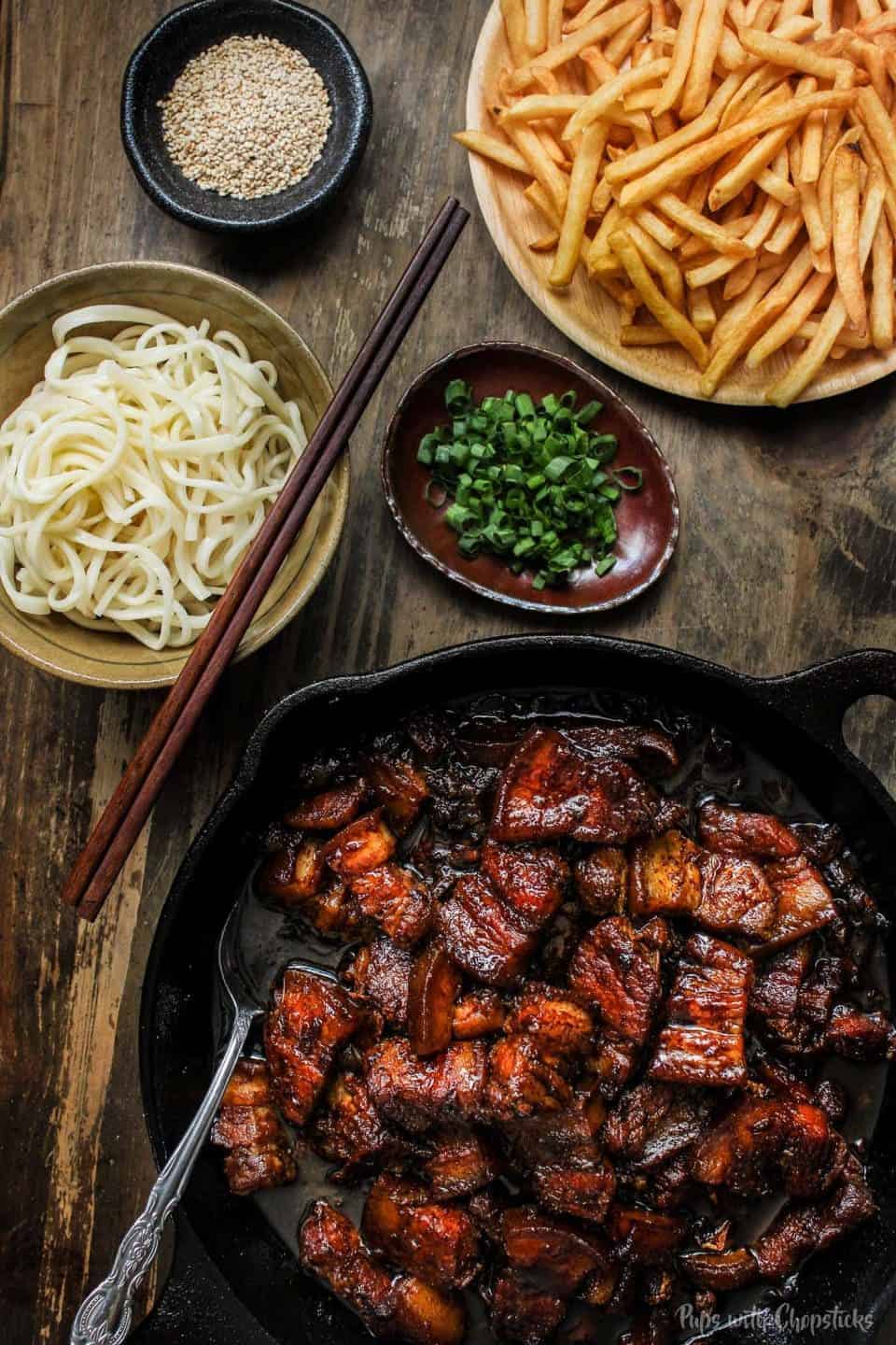 A pork belly skillet with noodles and chopsticks.