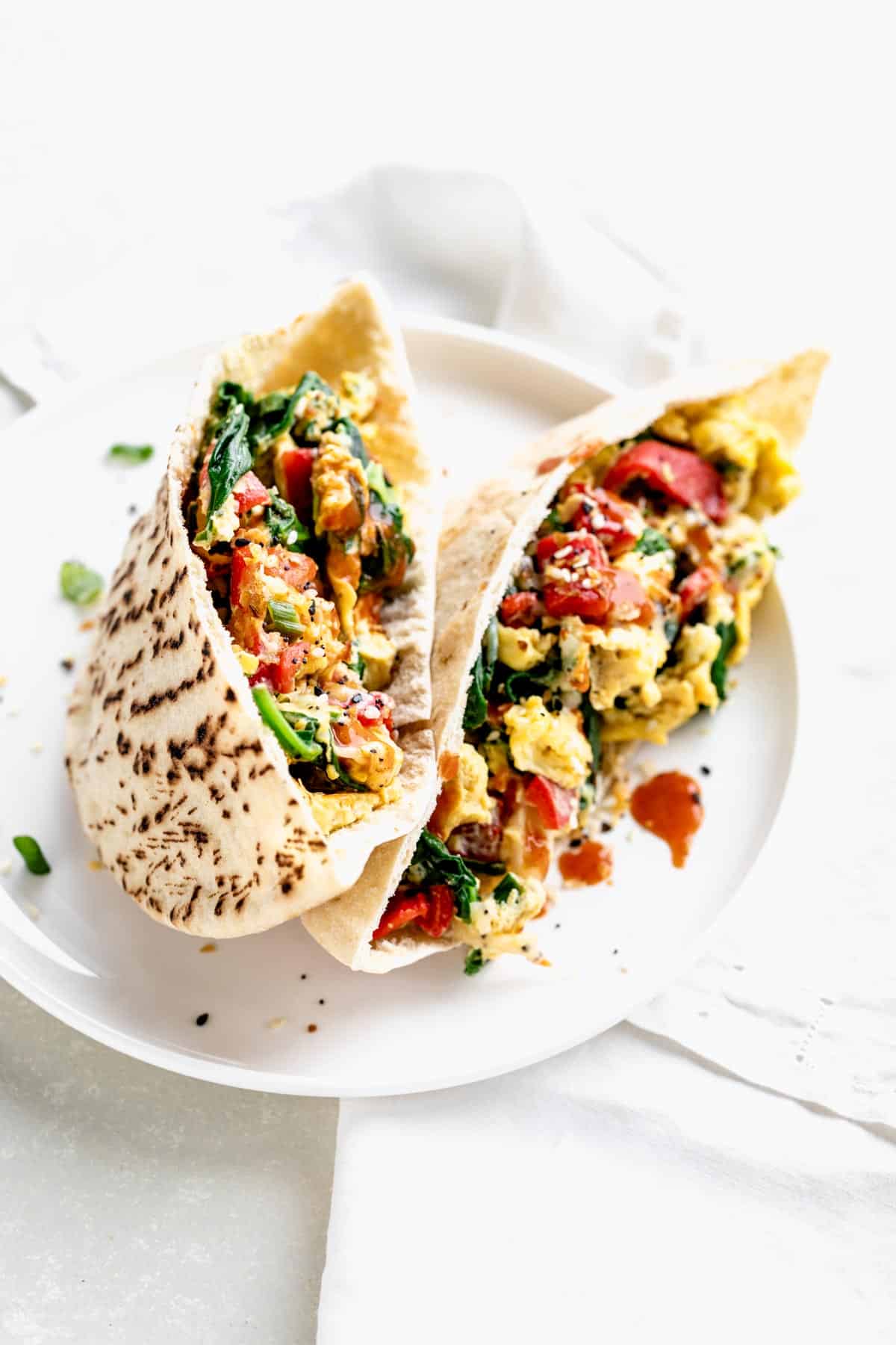 Two high protein breakfast burritos with spinach and eggs on a plate.