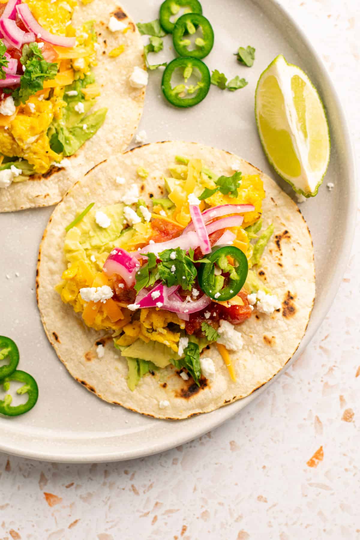 breakfast taco on a plate with lime wedge and jalapeno slices around. 
