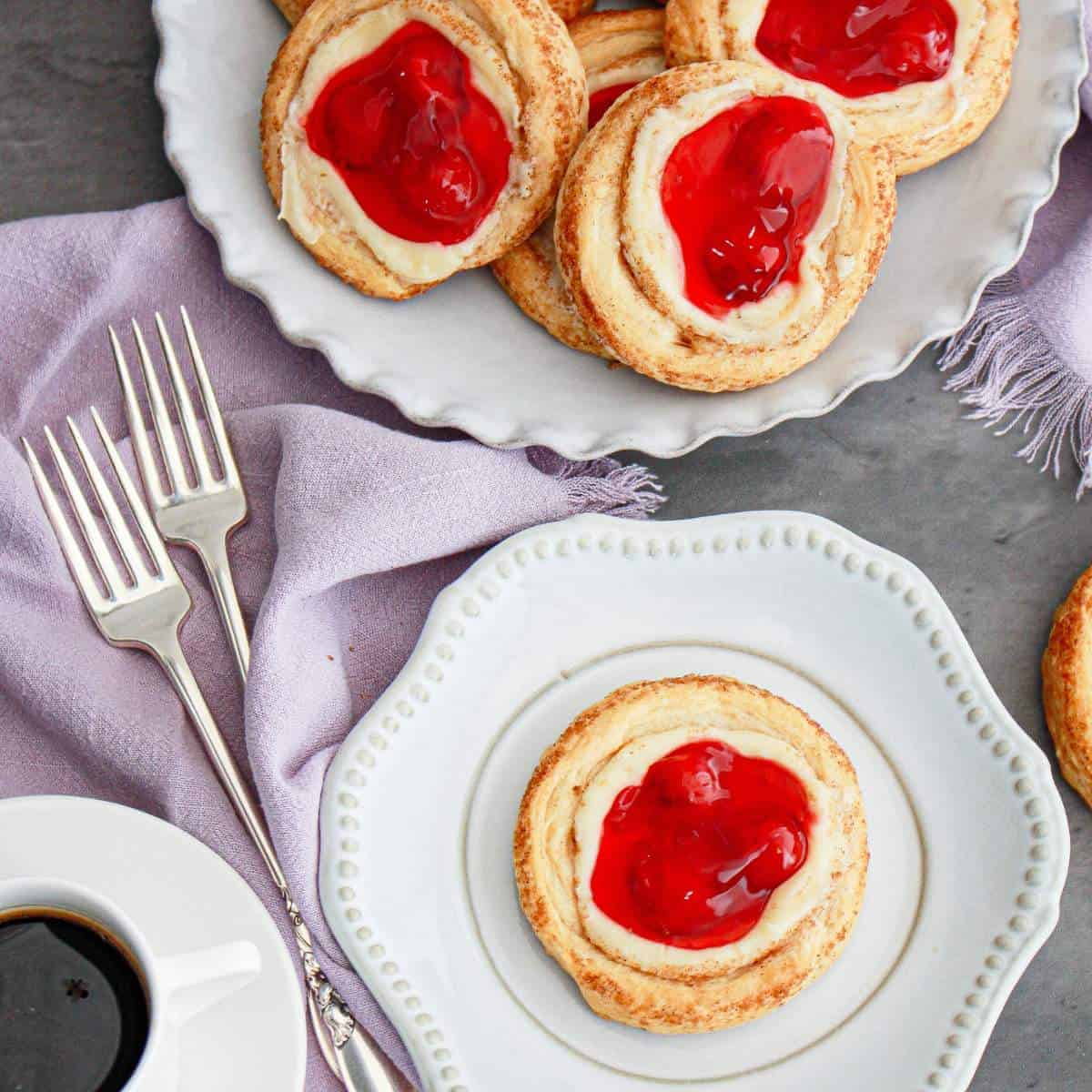 A plate of cherry cream cheese danishes made from crescent rolls on a table with a cup of coffee. 
