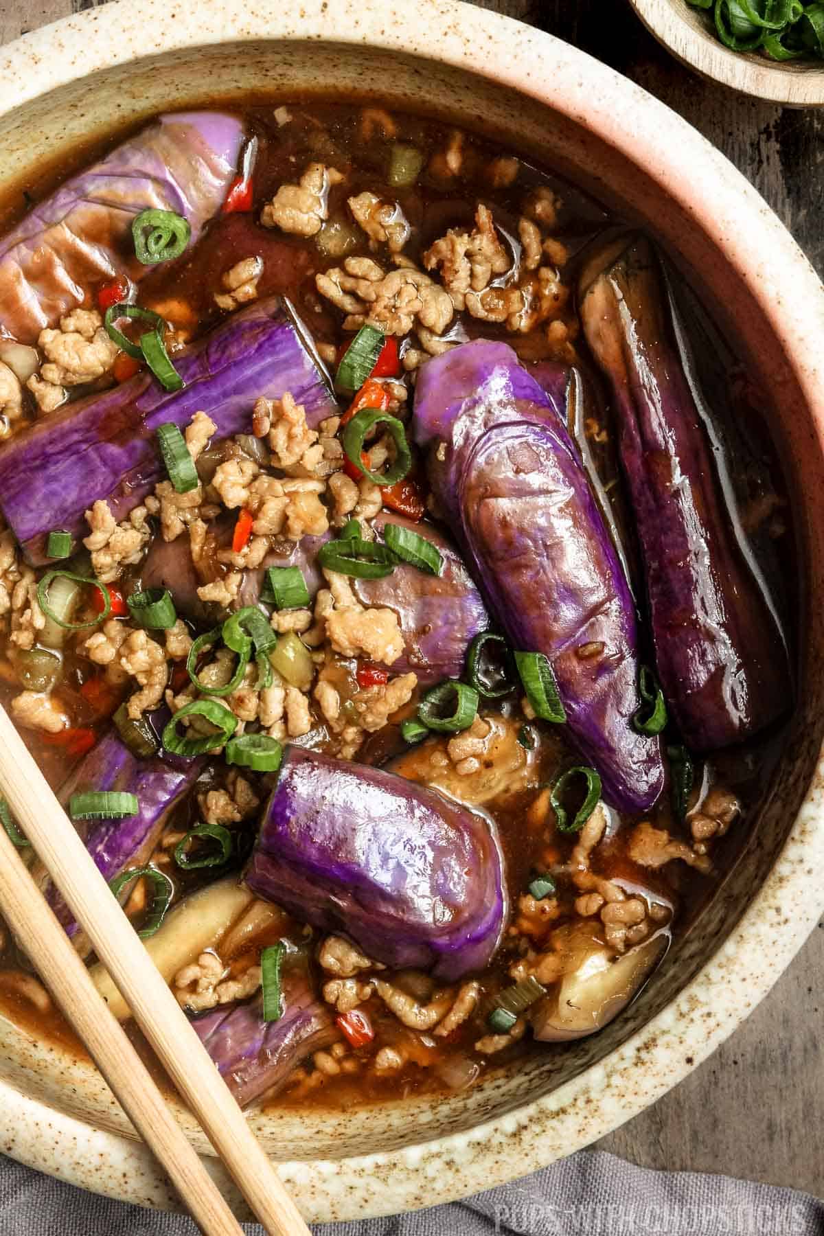 A bowl of eggplant in a sauce with chopsticks.