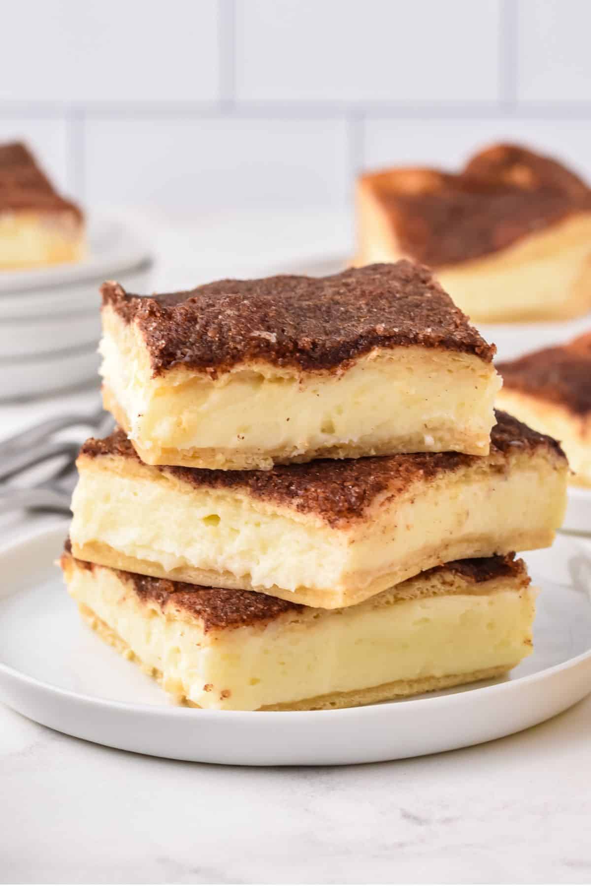 square cheesecake bars stacked on top of one another on a plate.
