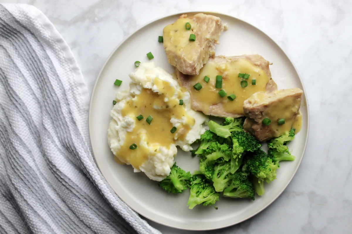Ranch pork chop gravy on a plate with sides of gravy covered mashed potatoes and steamed broccoli.
