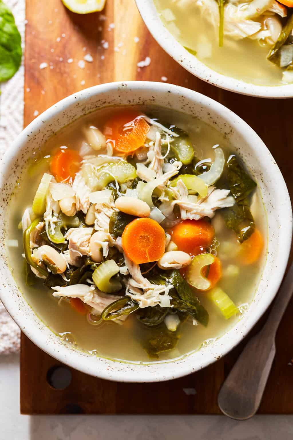 bowl of chicken soup with beans, spinach, and carrots / Tuscan Chicken Soup is something that you can enjoy year-round. This crockpot chicken soup recipe is so delicious and so simple. An easy Tuscan Soup to make at home, filled with so many good ingredients.