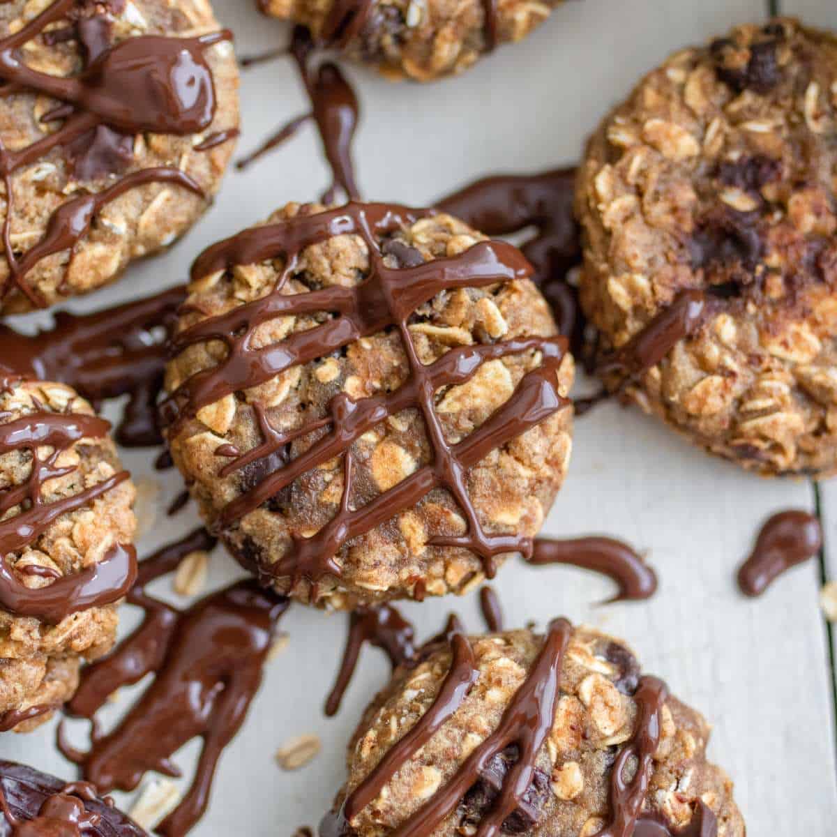 Unique chocolate drizzled oat cookies on a wooden table.