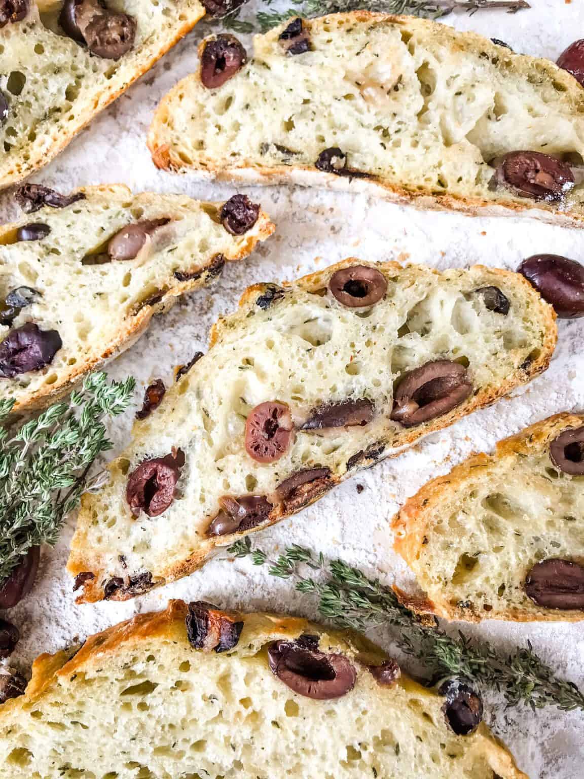Slices of olive bread spread out / Dutch Oven No Knead Rustic Thyme Olive Bread recipe is a homemade bread filled with kalamata olives and thyme (or rosemary). Simple to make Italian bread. #homemadebread #olivebread #dutchovenbread #nokneadbread
