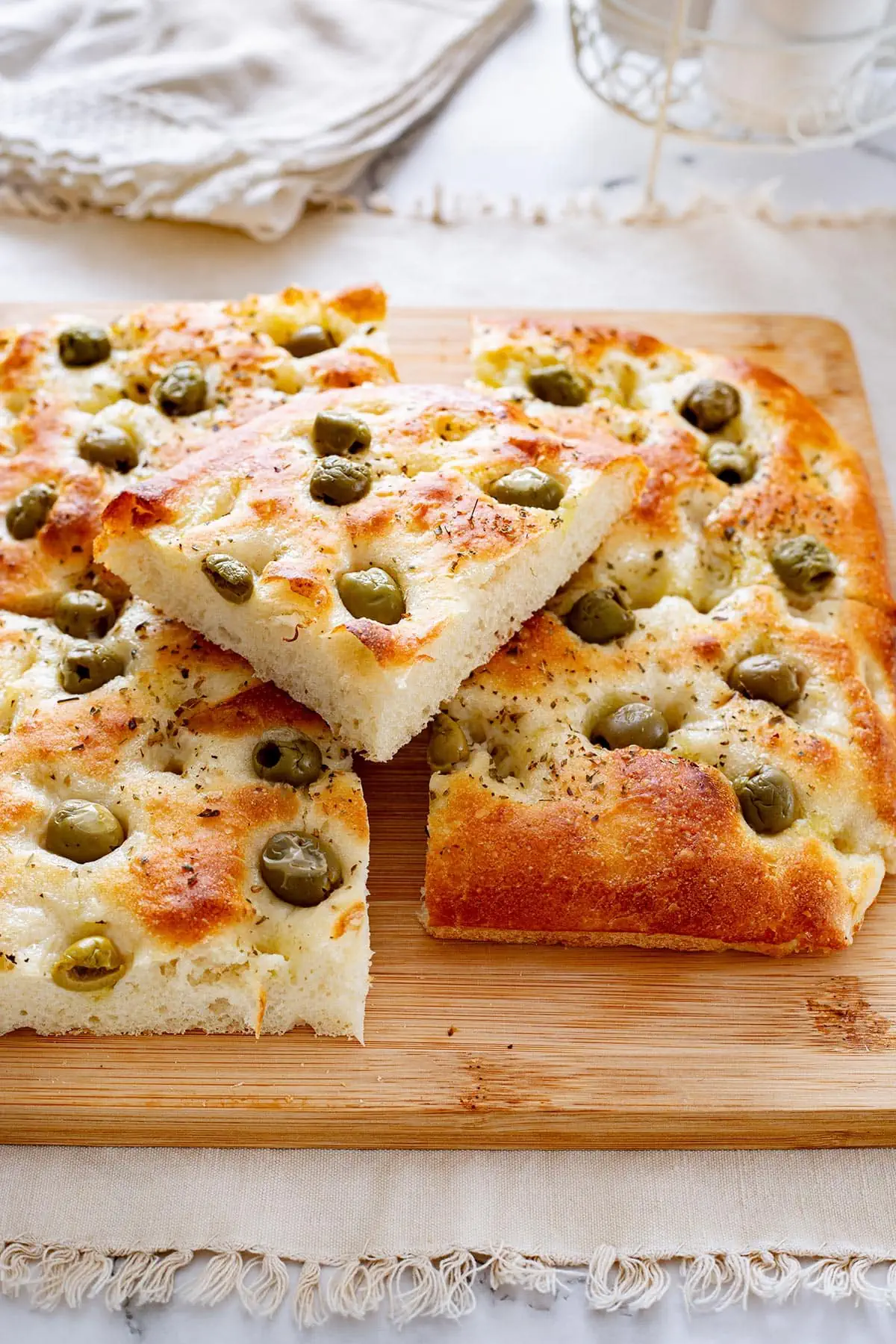 Fluffy focaccia con le olive cut into squares on a cutting board. 
