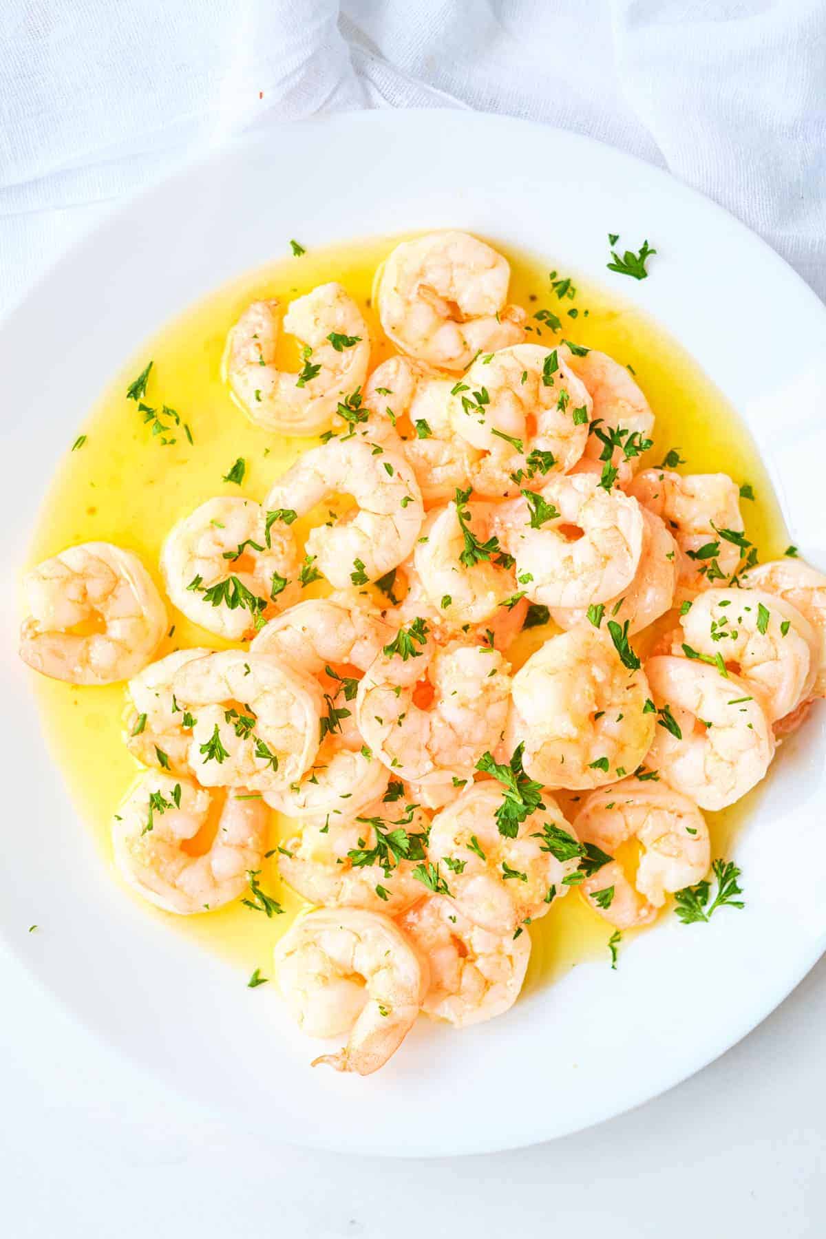 garlic butter shrimp on a plate with chopped herbs.
