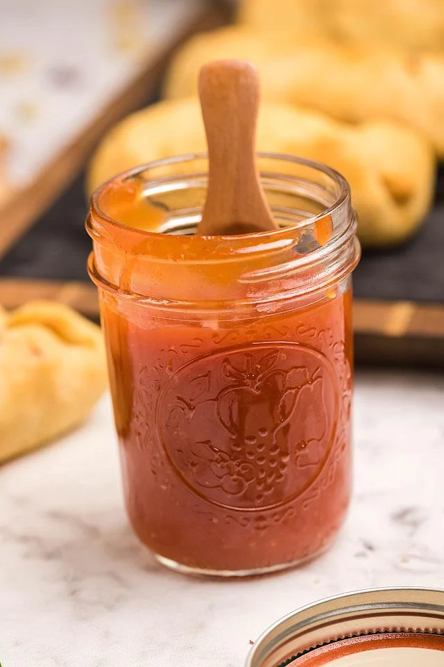 A jar of tomato sauce next to a wooden spoon.