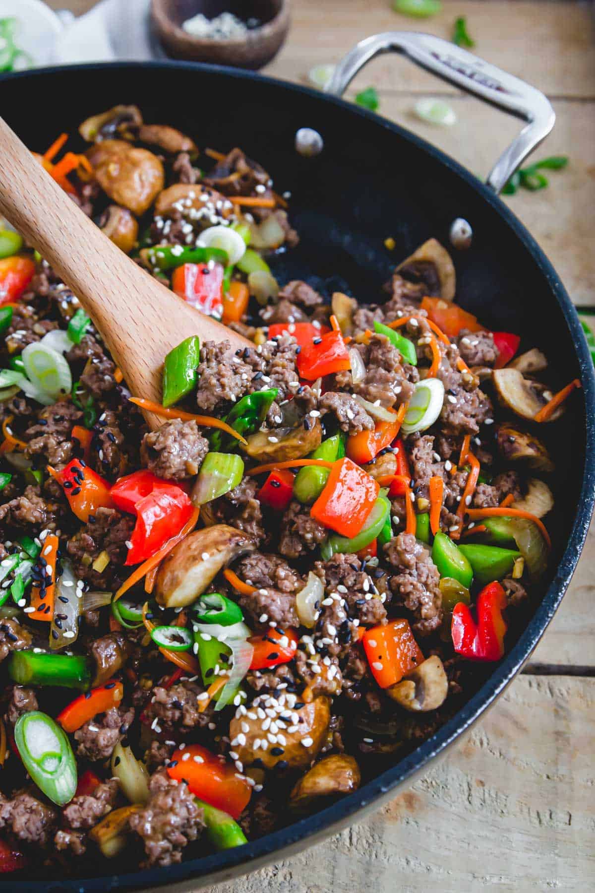 Ground beef stir fry in a skillet with a wooden spoon. 
