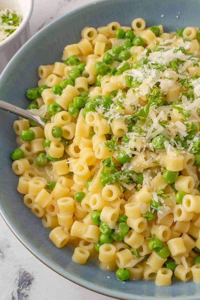 Pasta and peas in a blue bowl with a spoon. 
