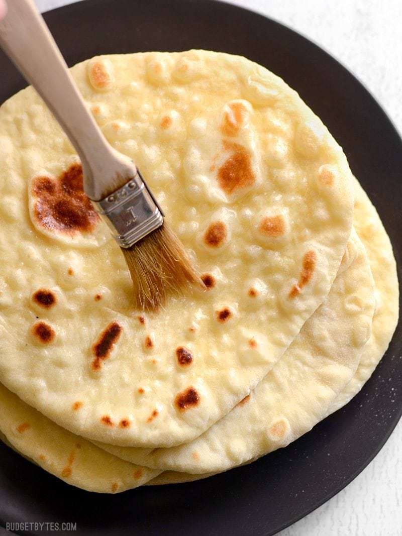Homemade naan bread being brushed with melted butter. / Soft, pillowy, homemade naan bread is easier to make than you think and it's great for sandwiches, pizza, dipping into soups and sauces, and more. 
