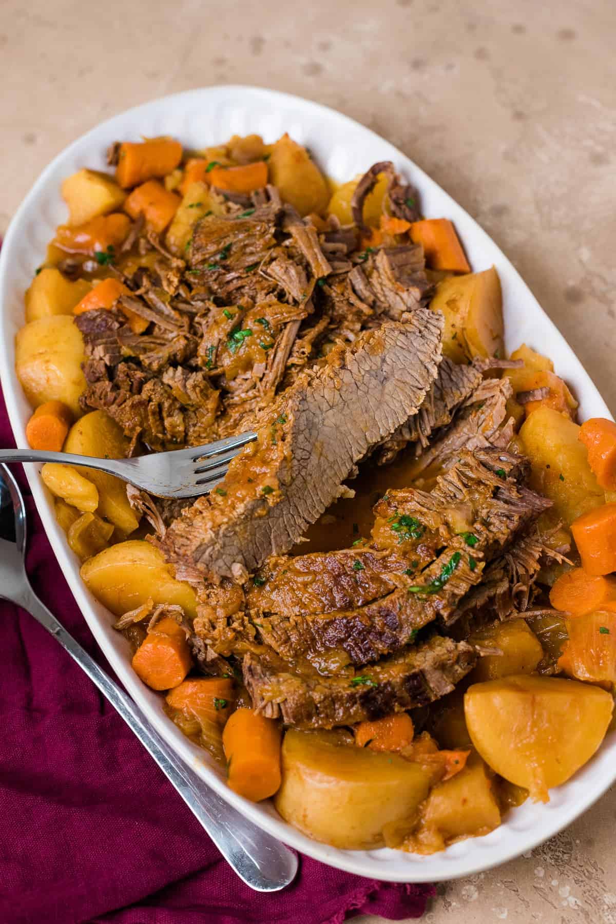 sliced instant pot brisket on a serving platter with carrots and potatoes and a fork grabbing a slice of brisket. 
