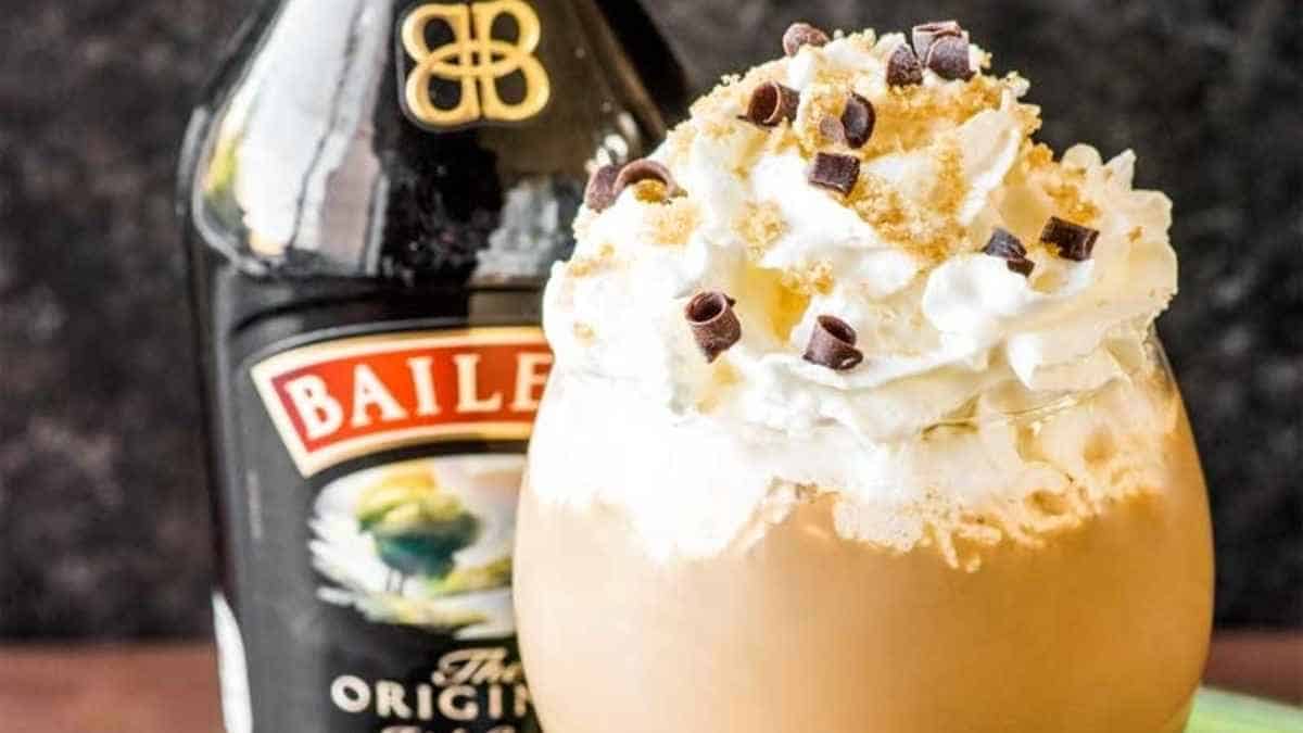 A bailey's irish coffee with whipped cream and a bottle of bailey's.