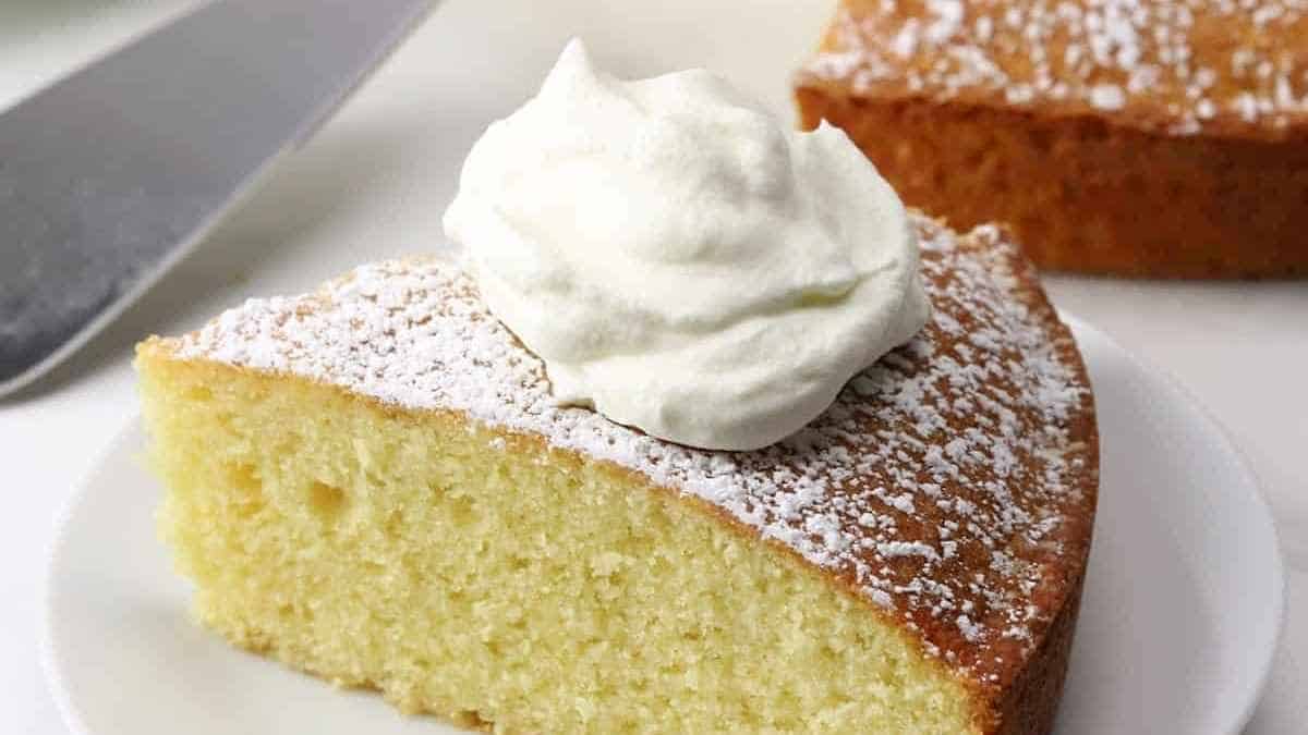 A slice of lemon cake on a plate with whipped cream.