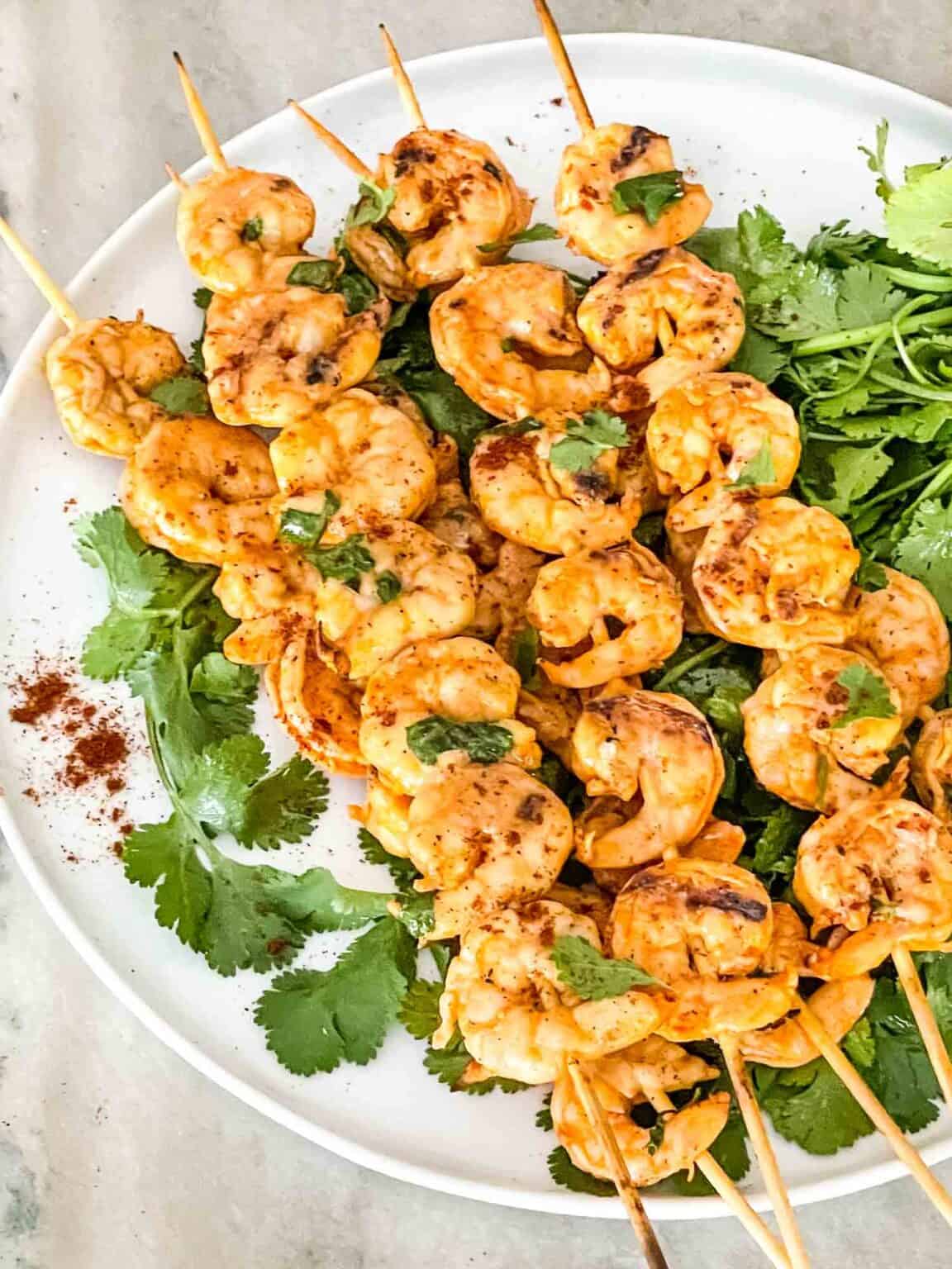 Mexican Grilled Shrimp skewers on cilantro on a white plate.
