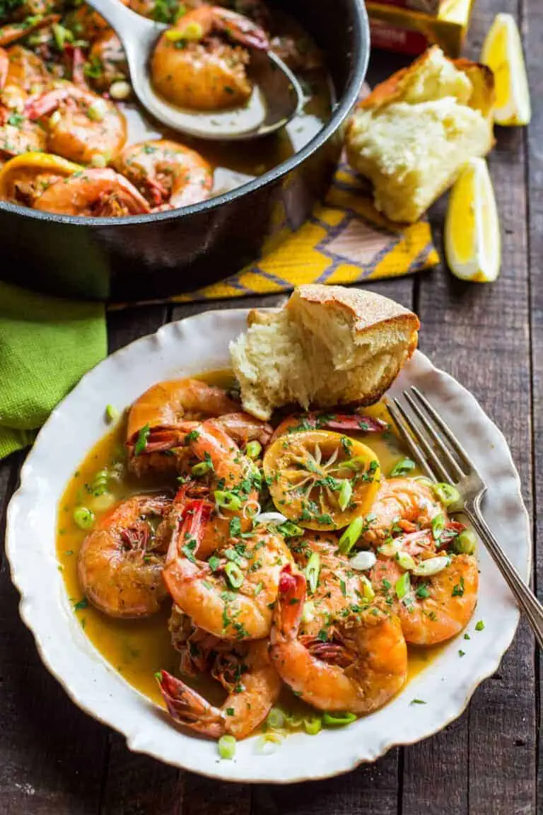 a white plate with shrimp, lemon and bread.
