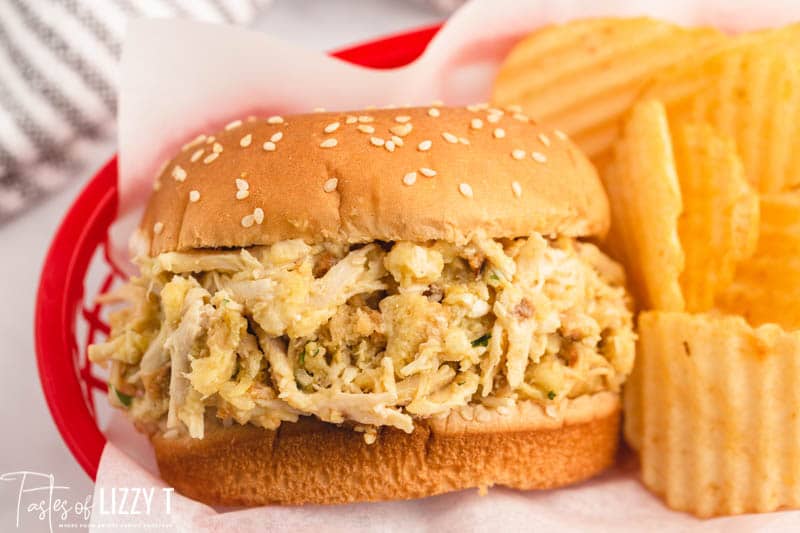a shredded chicken sandwich in a basket with chips.
