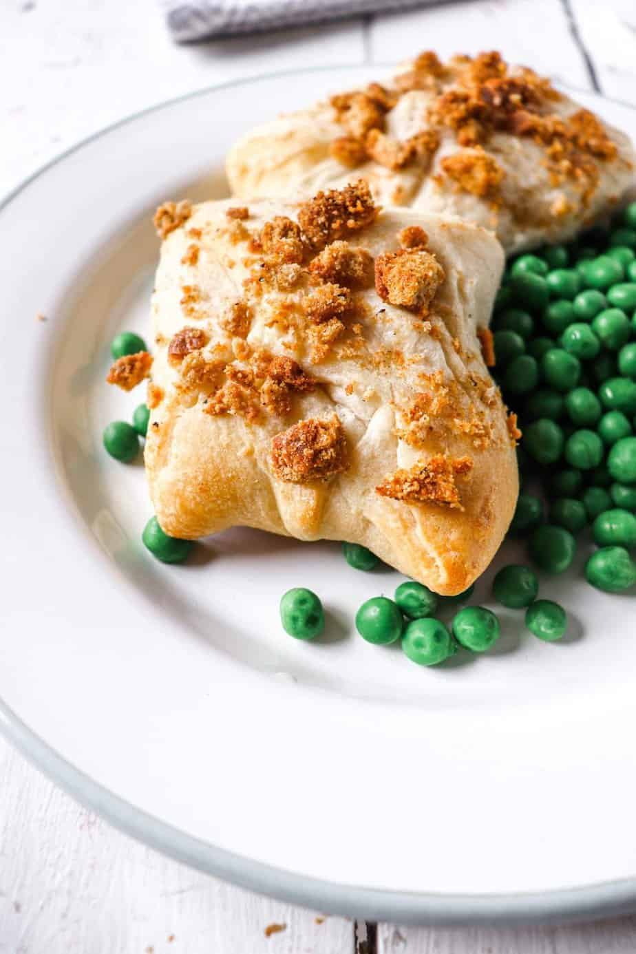 two chicken packets on a white plate with a bed of peas to the side.
