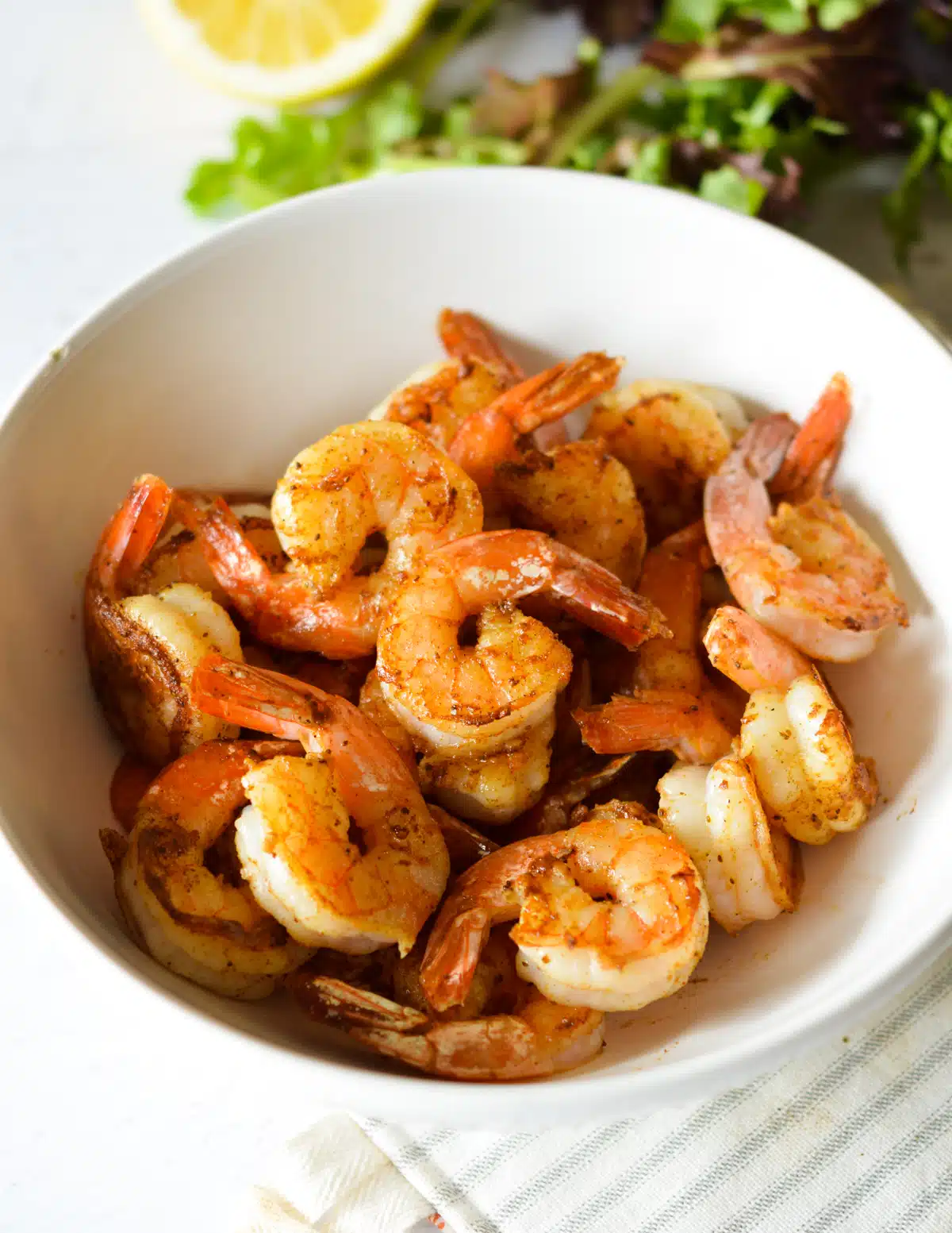 Grilled shrimp in a white bowl with lemon wedges.