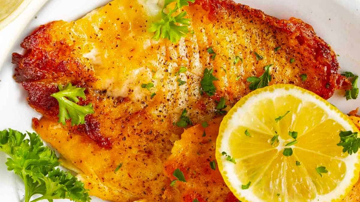 Fish fillets with lemon and parsley on a white plate.
