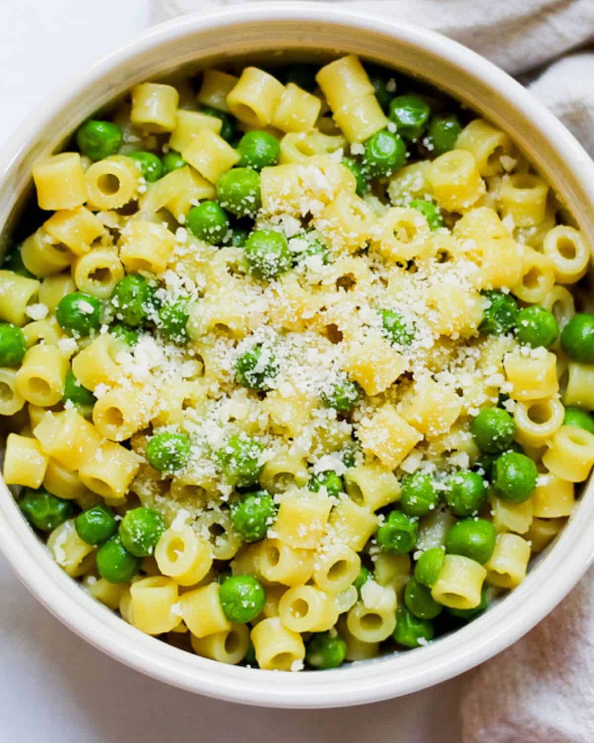 Ditalini pasta and green peas dish with grated Parmesan on top in a white bowl. 
