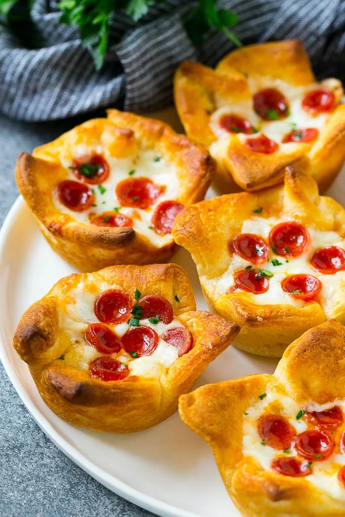 A plate of pizza muffins made with crescent roll dough, pizza sauce, melted cheese and mini pepperoni. / Pizza Muffins Recipe | Pizza Bites | Pizza Cups | Pizza Appetizer #pizza #appetizer #dinneratthezoo
