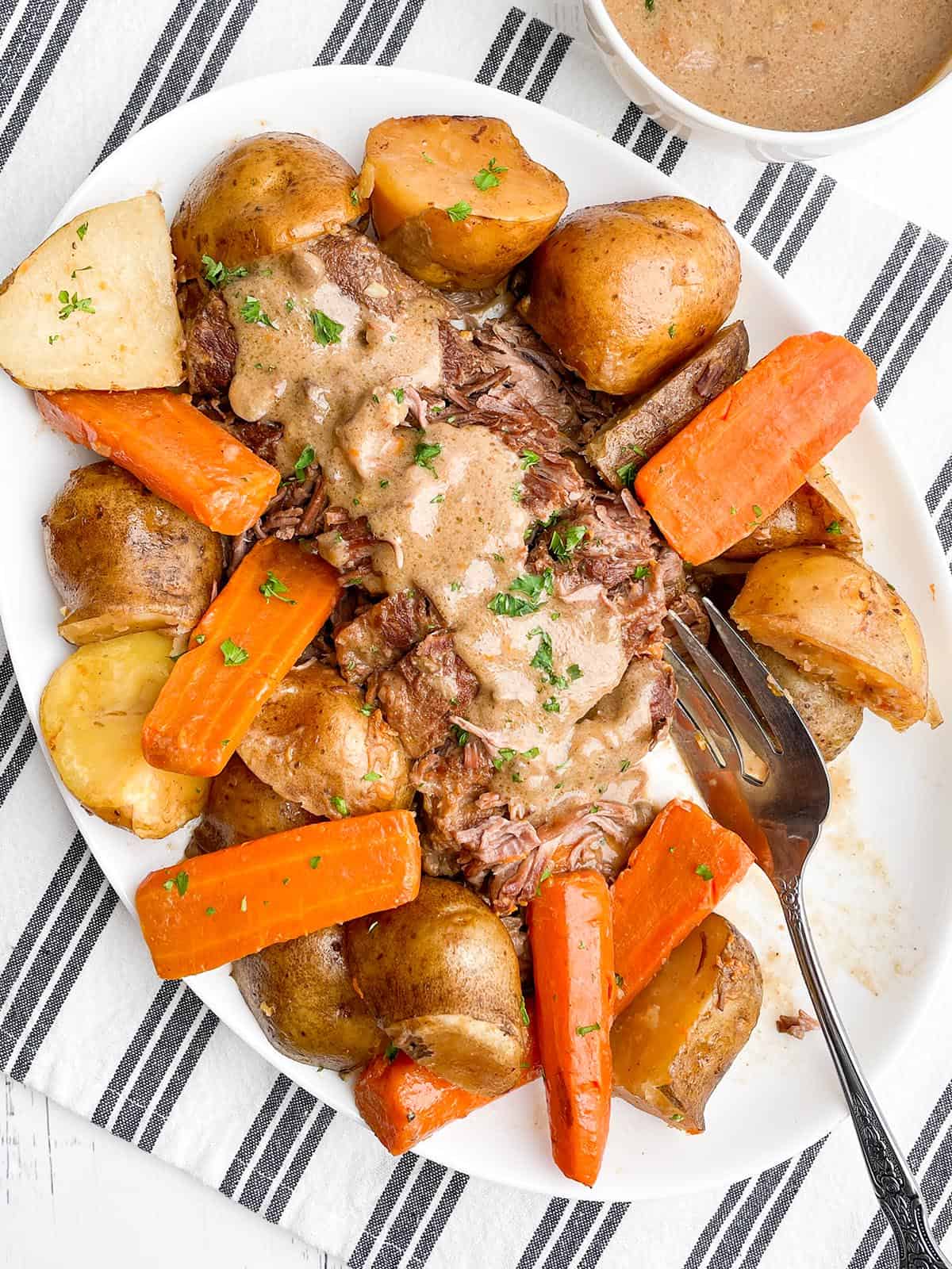 Pot roast with onion soup mix, potatoes, and carrots on a white platter. 
