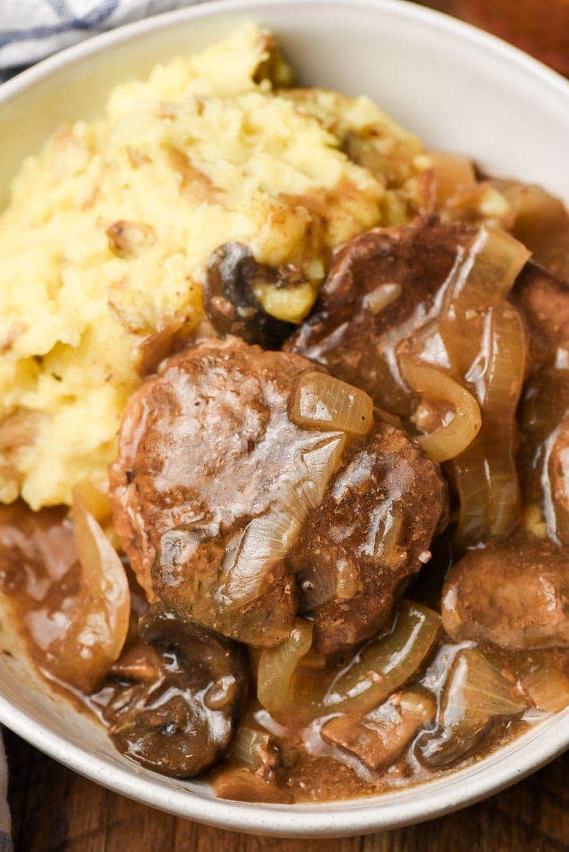round steaks with gravy in a bowl with mashed potatoes.
