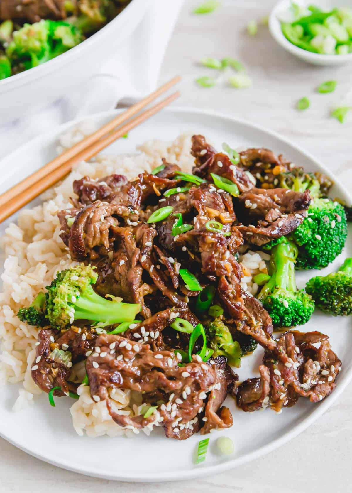 A plate of shaved beef and broccoli with chopsticks.