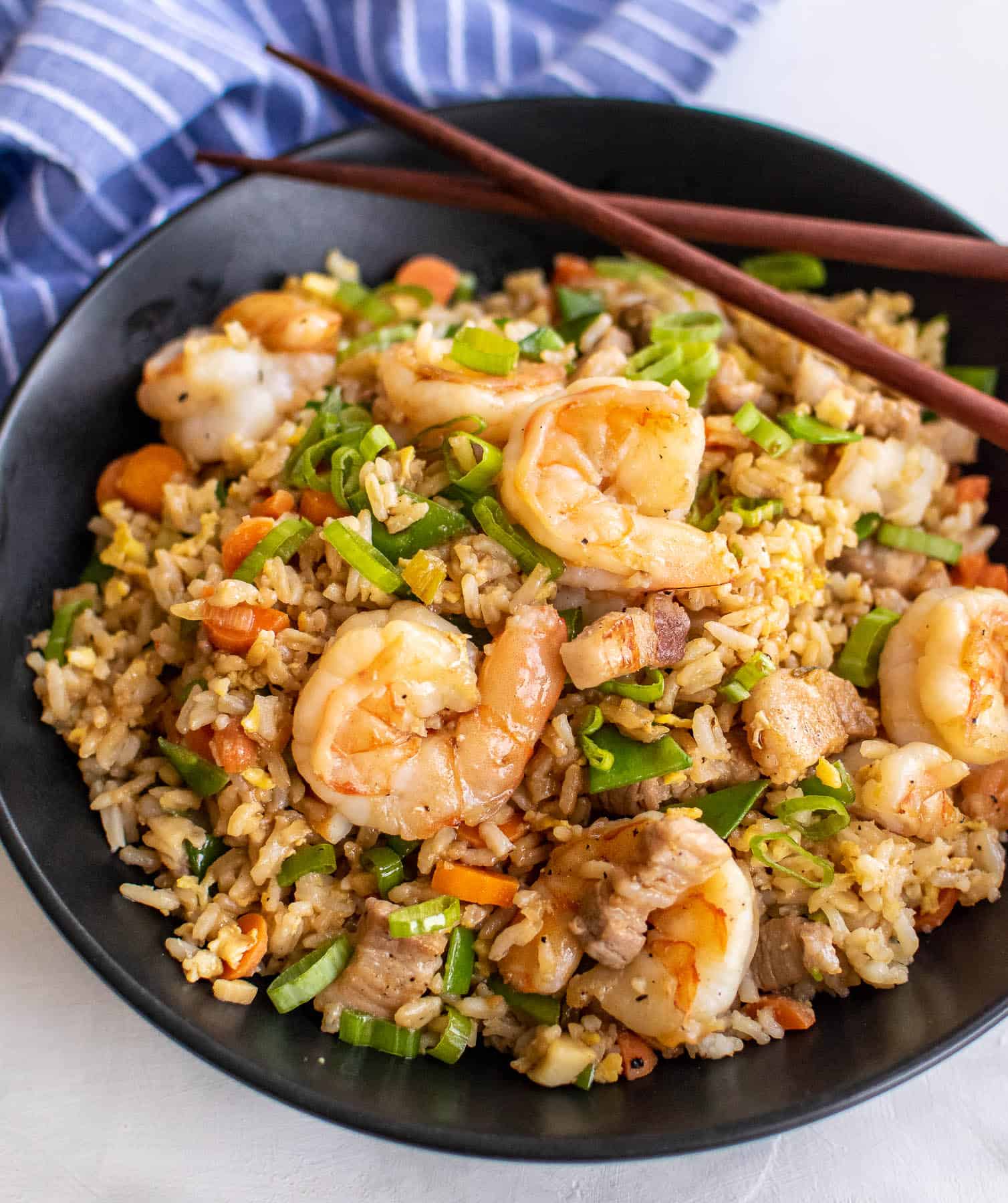 Shrimp fried rice with pork belly in a black bowl with chopsticks.
