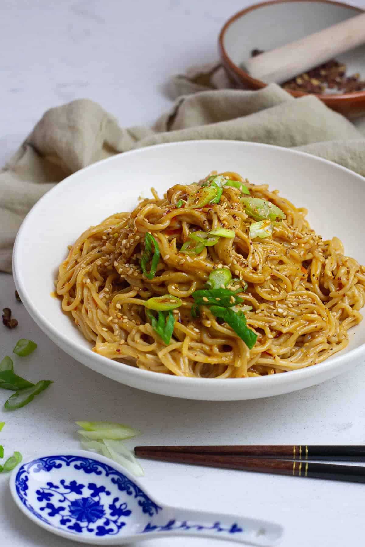 A bowl of noodles with sesame seeds and green onions.
