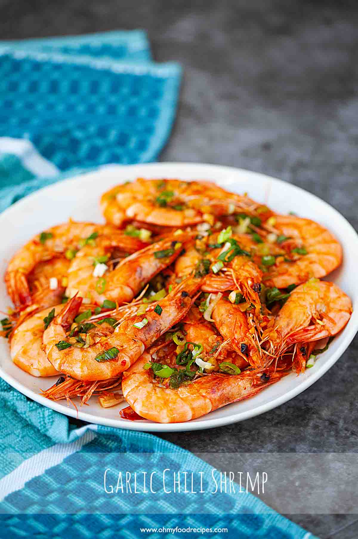 Asian style chili garlic shrimp on an oval white plate with blue towel.
