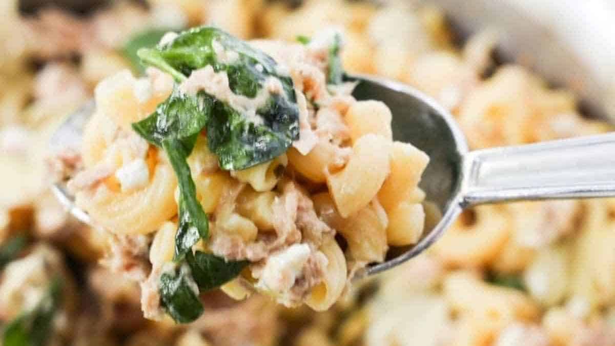 A spoonful of creamy pasta with spinach and chunks of meat, served from a skillet.