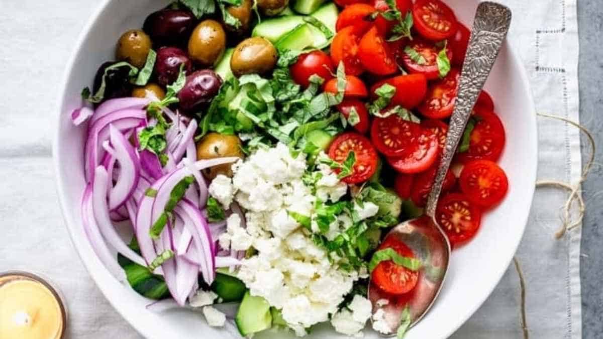 A bowl of greek salad with olives, tomatoes, onions and feta cheese.