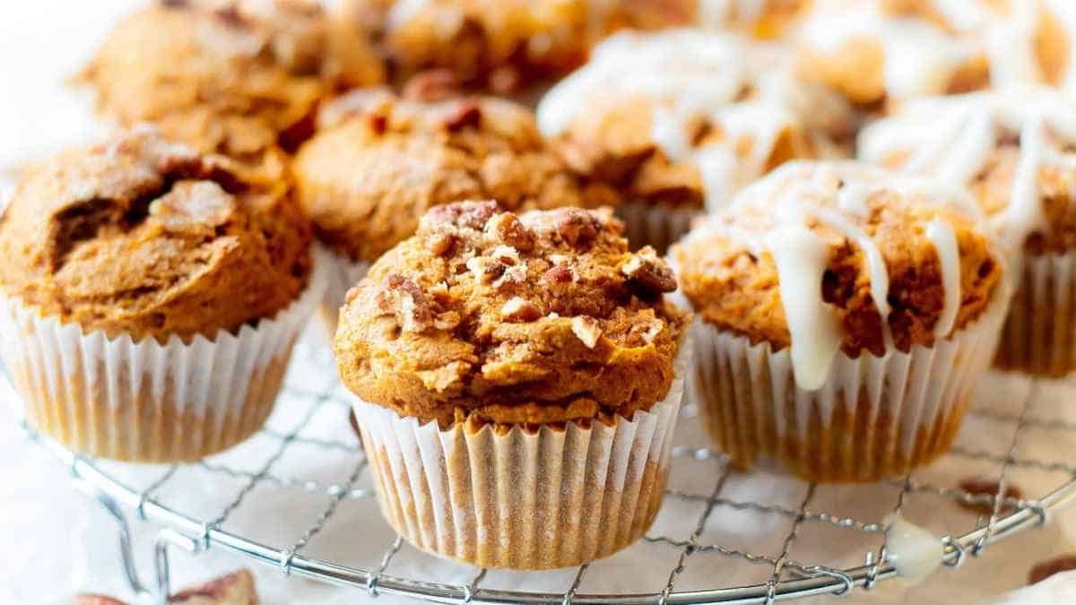 Freshly baked muffins on a cooling rack with some topped with nuts and others with a glaze.