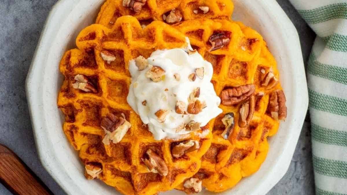 A plate of waffles with whipped cream and pecans.