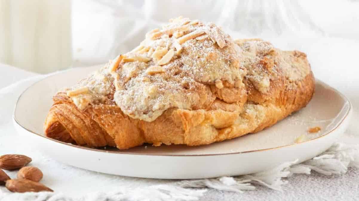 Almond croissant on a plate with a glass of milk in the background.