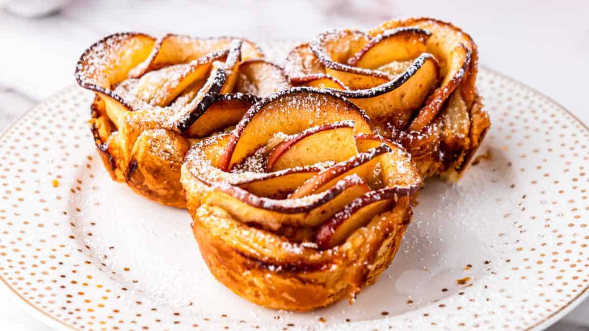 Three apple rose pastries dusted with powdered sugar on a dotted plate.