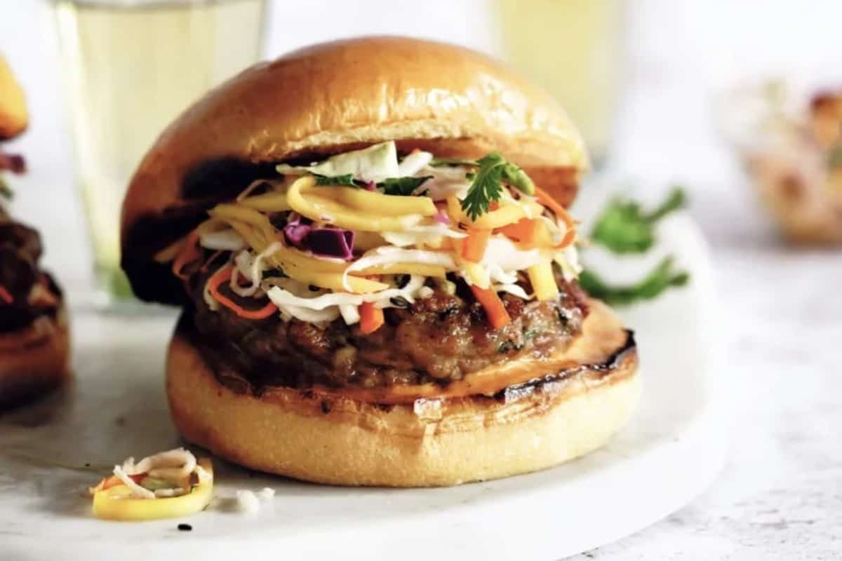 A juicy burger topped with slaw and fresh herbs, served on a brioche bun.