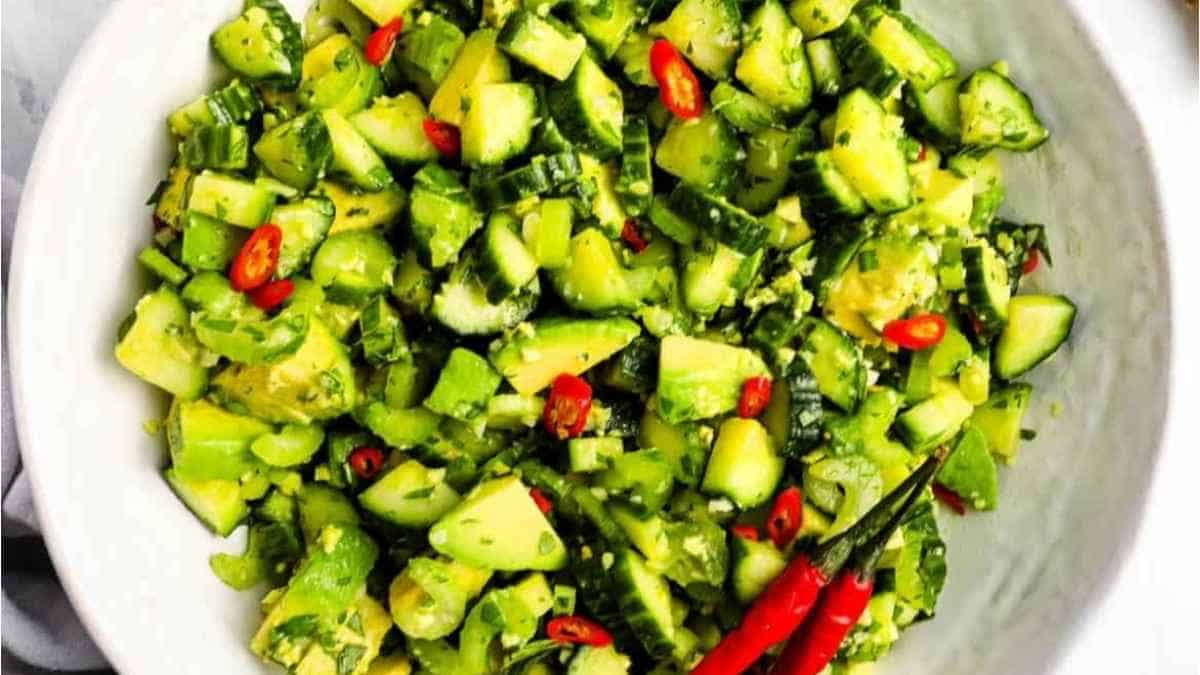 Cucumber salad in a white bowl with chili peppers.