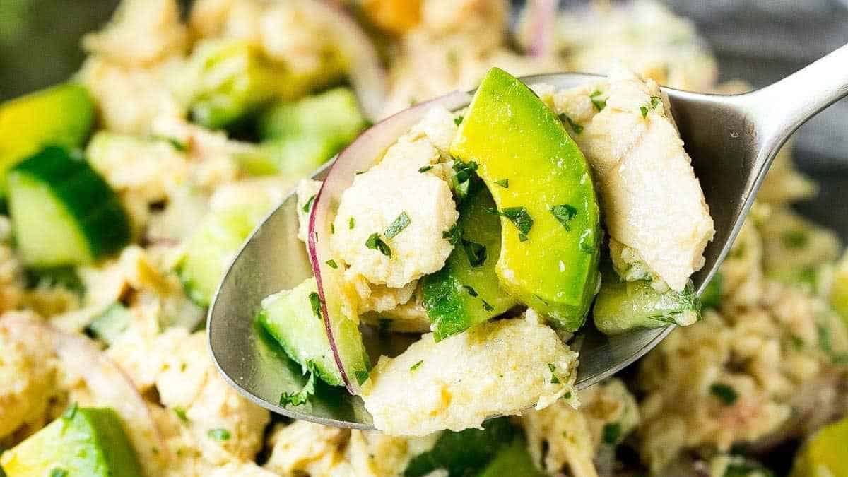 A spoonful of chicken salad with avocado and herbs.