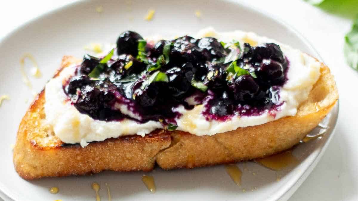 A slice of french toast topped with cream cheese and blueberry compote, garnished with mint leaves.