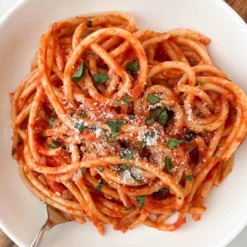 A bowl of spaghetti with tomato sauce and a sprinkle of cheese and herbs.