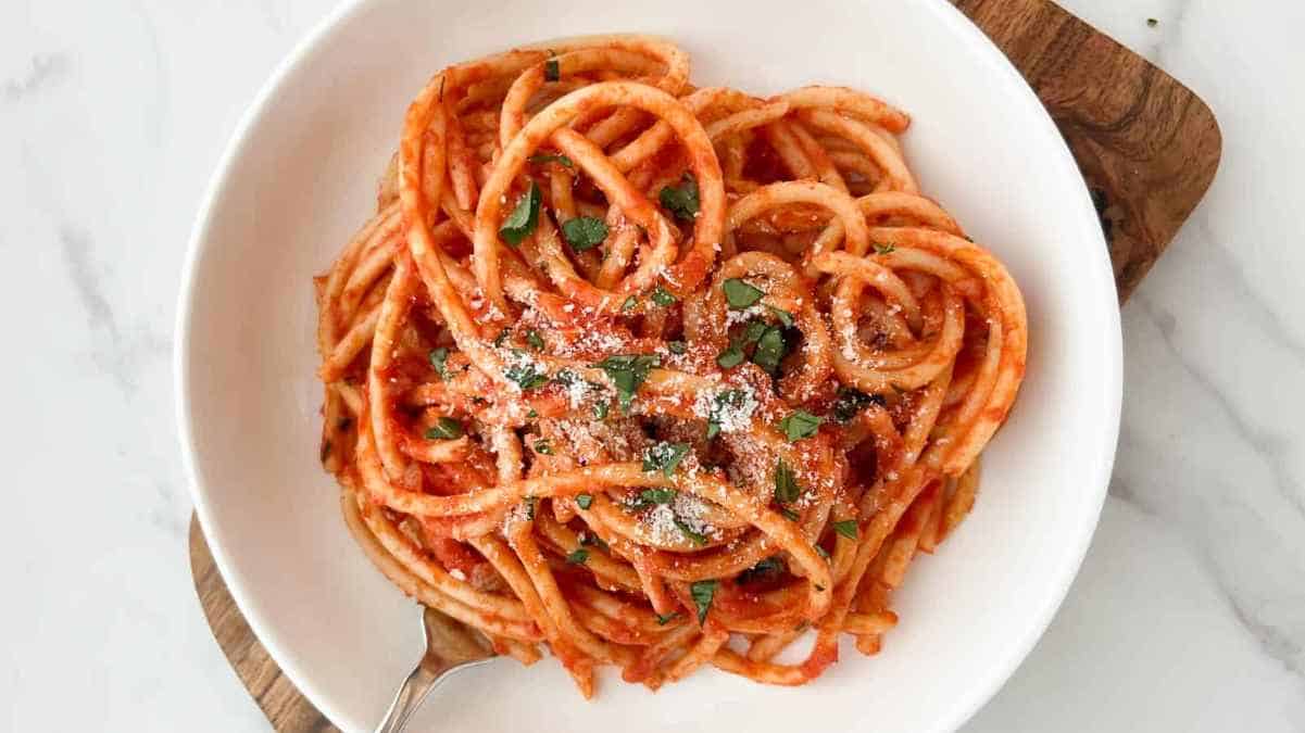 A bowl of spaghetti with tomato sauce and a sprinkle of cheese and herbs.