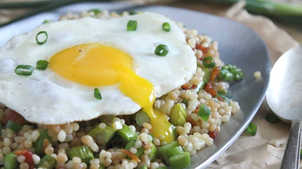 Fried egg atop a bed of grains and vegetables, sprinkled with chopped green onions.