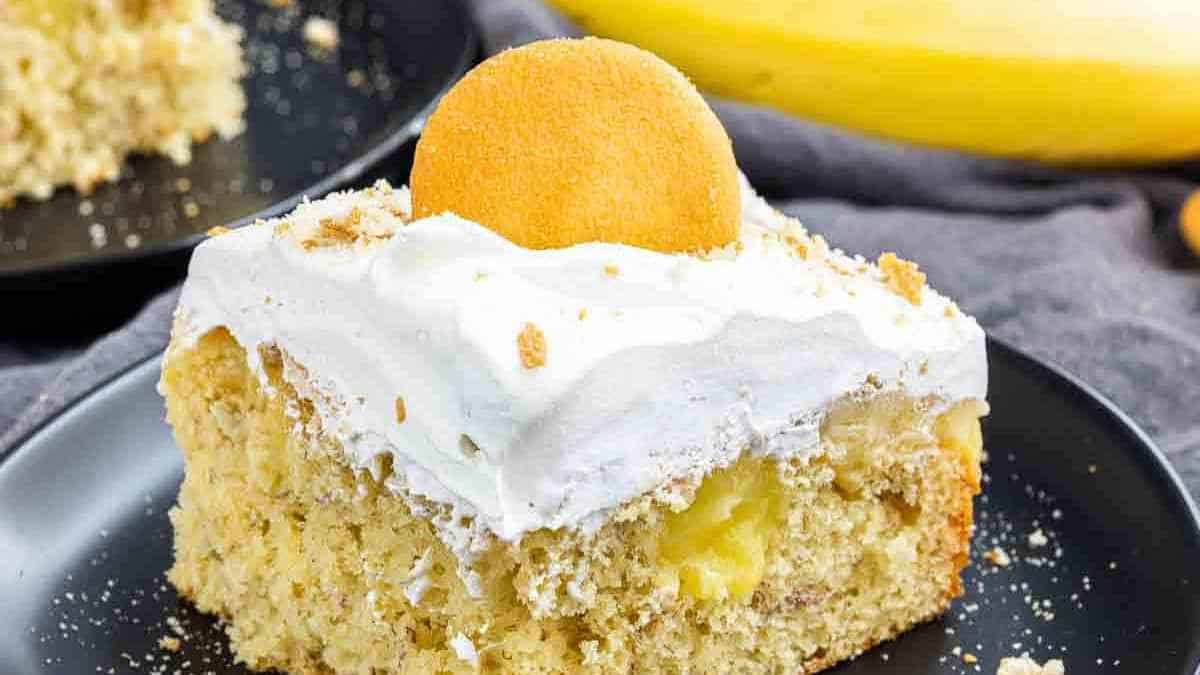 A slice of creamy, layered dessert topped with whipped cream and a cookie on a black plate.