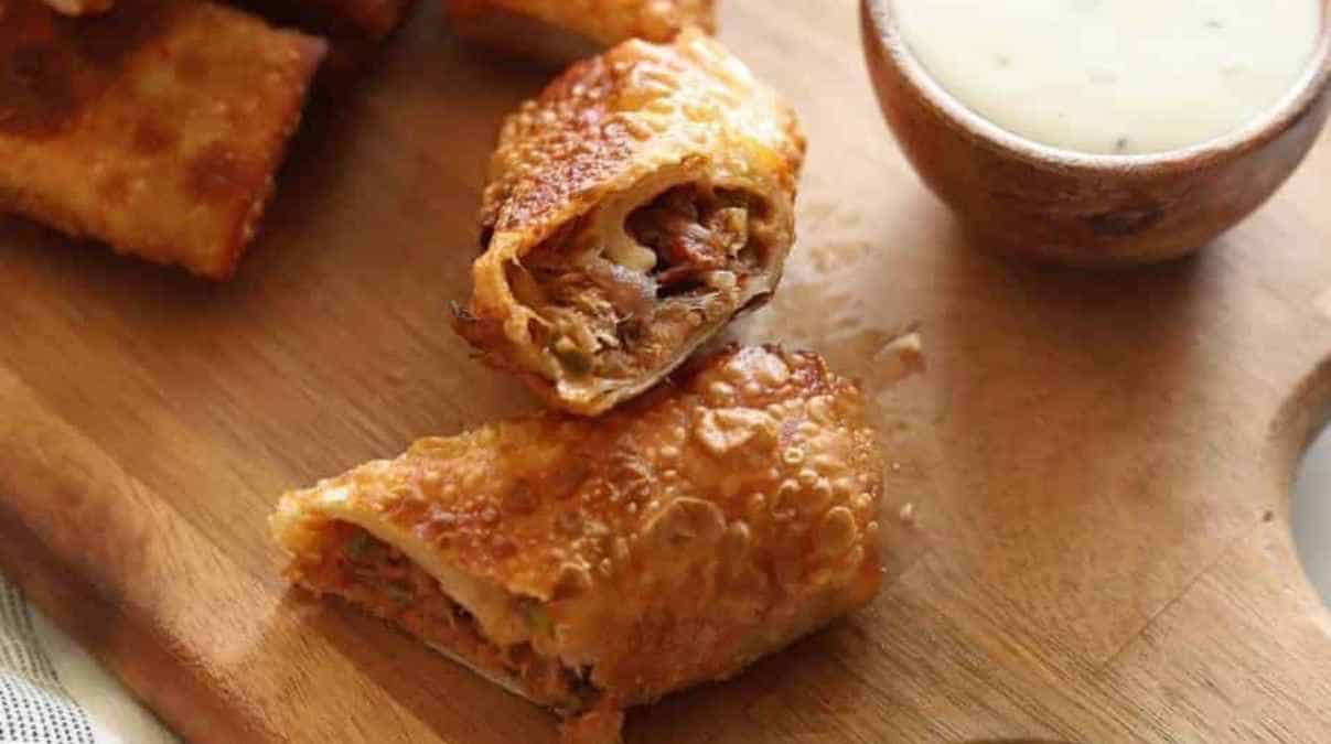 Golden-brown fried egg rolls cut open, served with dipping sauce.